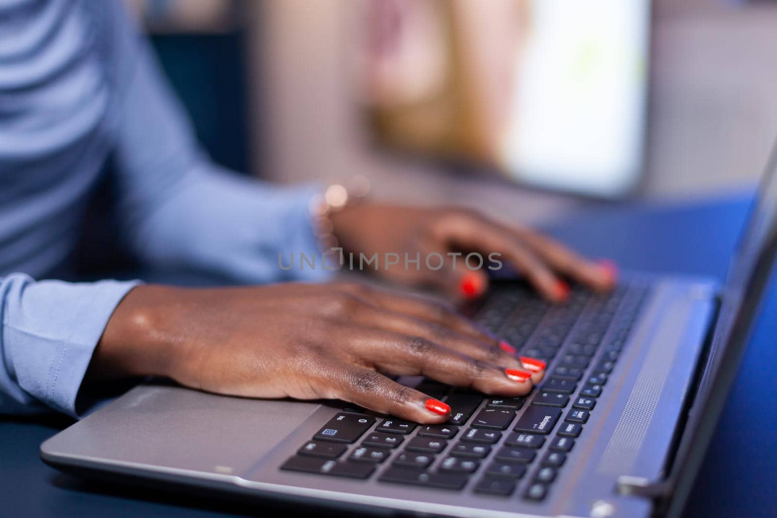 Close up of busy african woman typing on keyboard while she sits at home office. Employee using modern technology network wireless doing overtime.