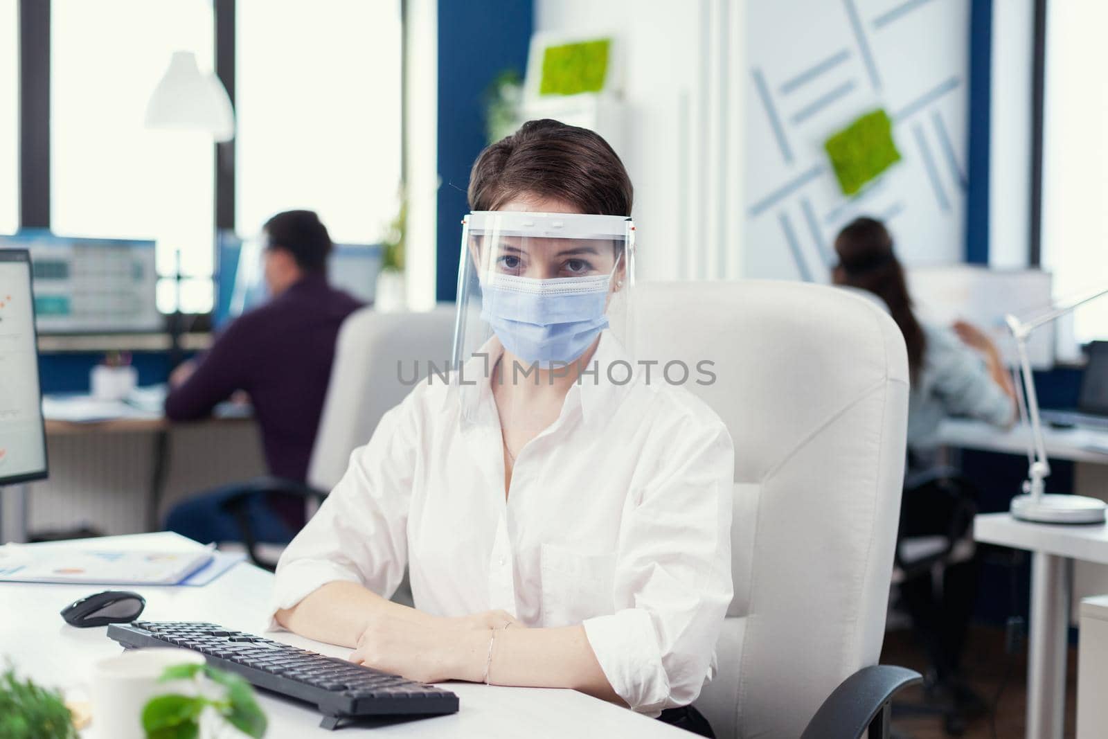 Female entrepreneur wearing face mask against covid19 as safety precaution at workplace Business team working in financial company respecting social distance during global pandemic.
