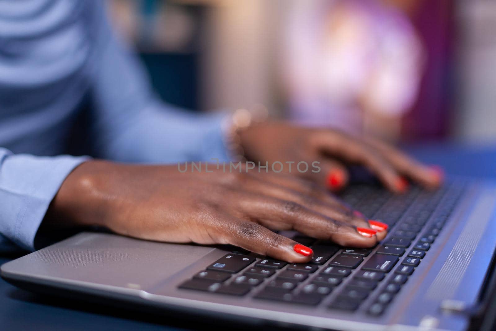 Close up of dark skinned business woman hand typing email n laptop computer from home office late at night. Employee using modern technology network wireless doing overtime.