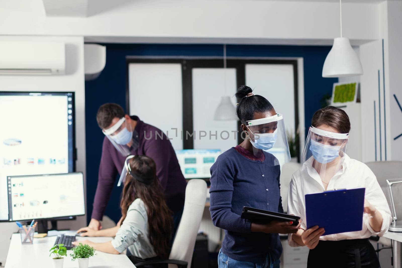 African project manager speaking with employee wearing face mask against covid19. Multiethnic business team working respecting social distance during global pandemic with coronavirus.