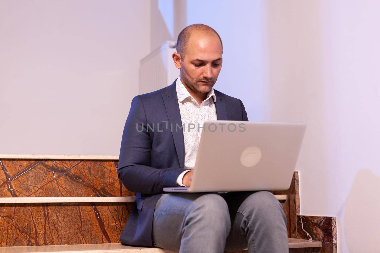 Stressed exahusted businessman working on business deadline using laptop. Confident corporate entrepreneur using laptop doing overtime sitting on stairwell.