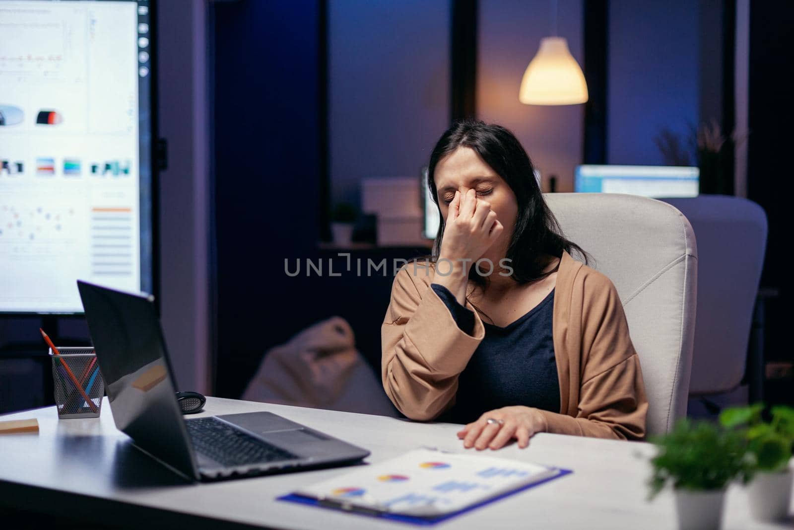 Portrait of freelancer having a headache feeling overworked because of job deadline. Employee falling asleep while working late at night alone in the office for important company project.