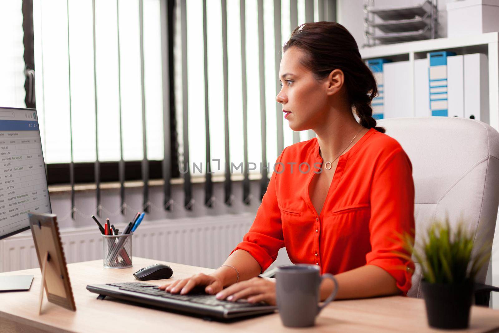 Businesswoman managerworking on professional finance expertise wearing red. Successful concentrated employer with busy carreer sitting at desk in office using modern pc.
