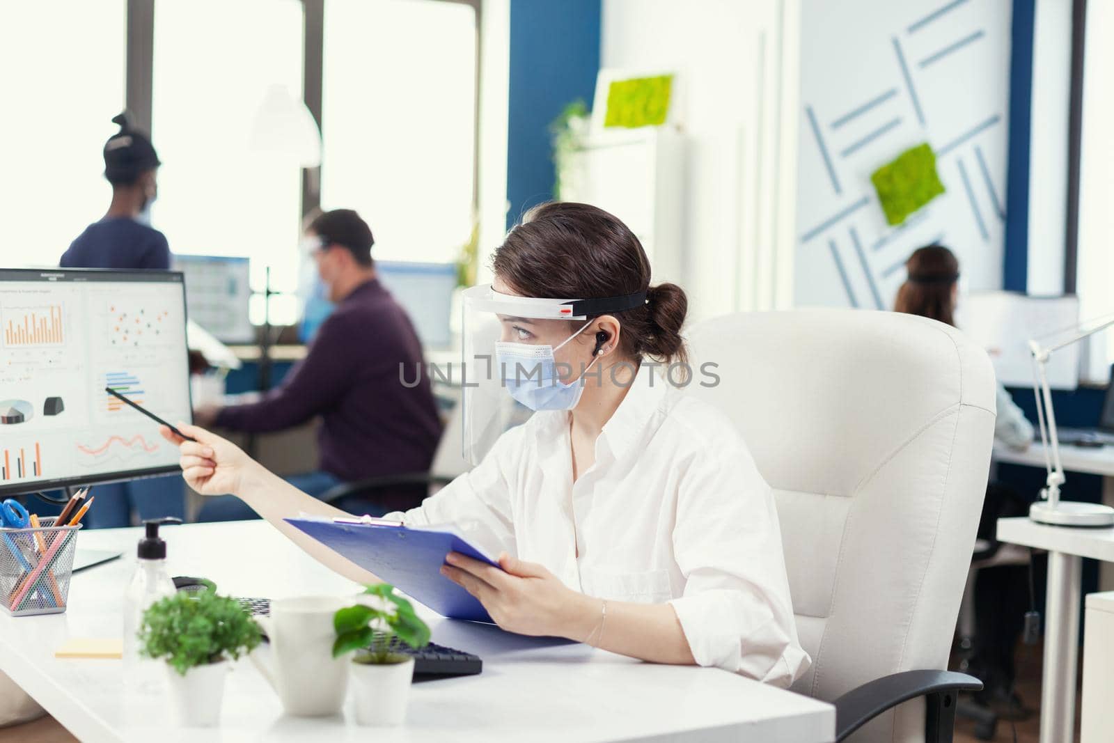 Manager wearing protection against covid 19 during global pandemic. Employees with visors working in corporate company workspace respecting social distance analysing data and graphs.