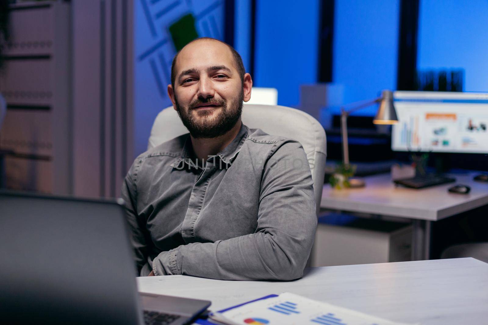 Confident entrepreneur looking confident looking at camera in empy office. Smart businessman sitting at his workplace in the course of late night hours doing his job.