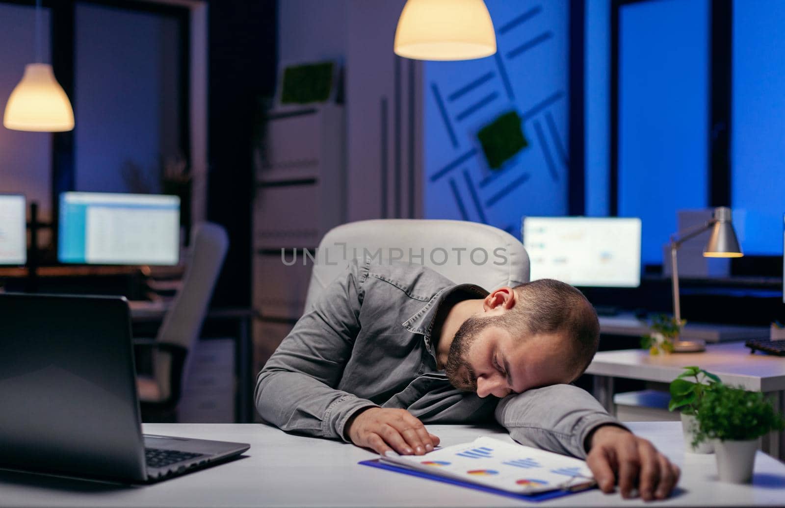 Tired businessman sleeping in his workplace on desk. Workaholic employee falling asleep because of while working late at night alone in the office for important company project.