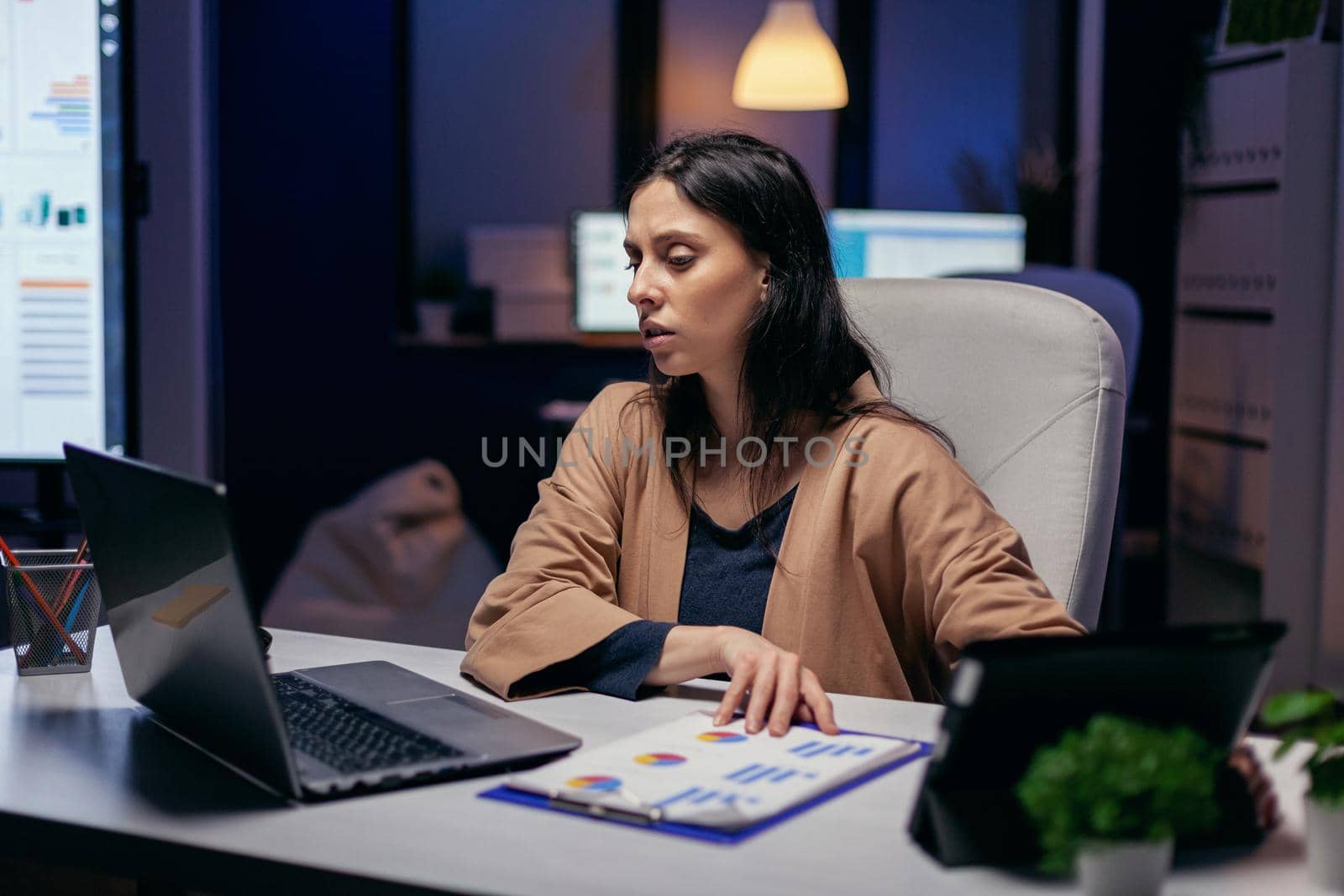 Entrepreneur reading project deadline for important client using tablet pc and laptop. Business woman working overtime at the office to finish a corporate job using tablet pc.