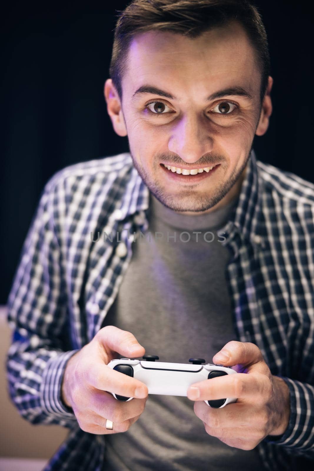 Caucasian guy addicted to tv entertainment. Male holding joystick control having fun laughing on couch indoors. Man in casual wear sitting on sofa and playing video game in home living room.