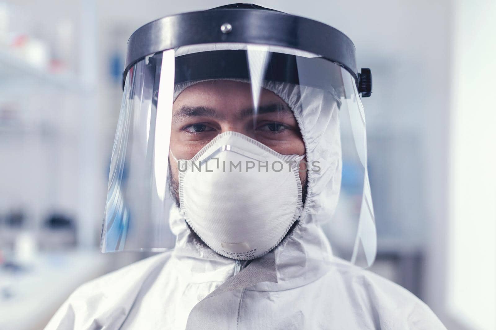 Tired healthcare scientist loooking at camera wearing ppe suit with face shield by DCStudio