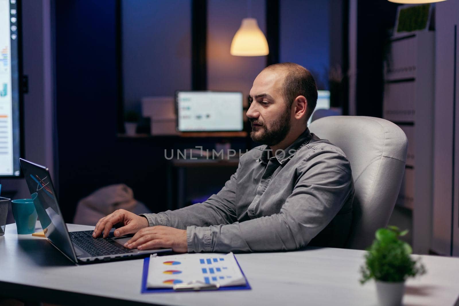 Concentrated young businessman working in office alone at night. Smart businessman sitting at his workplace in the course of late night hours doing his job.