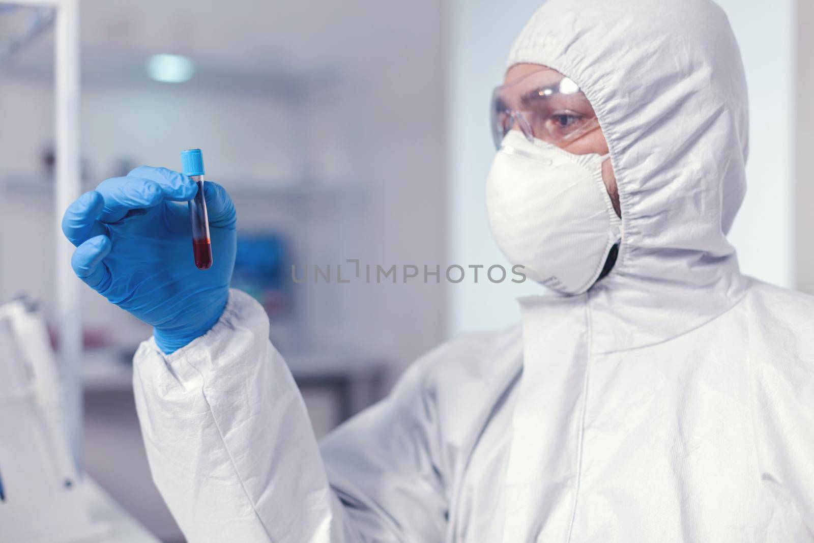 Medical engineer looking at sample of blood in tube wearing protection suit. Doctor working with various bacteria and tissue, pharmaceutical research for antibiotics against covid19.