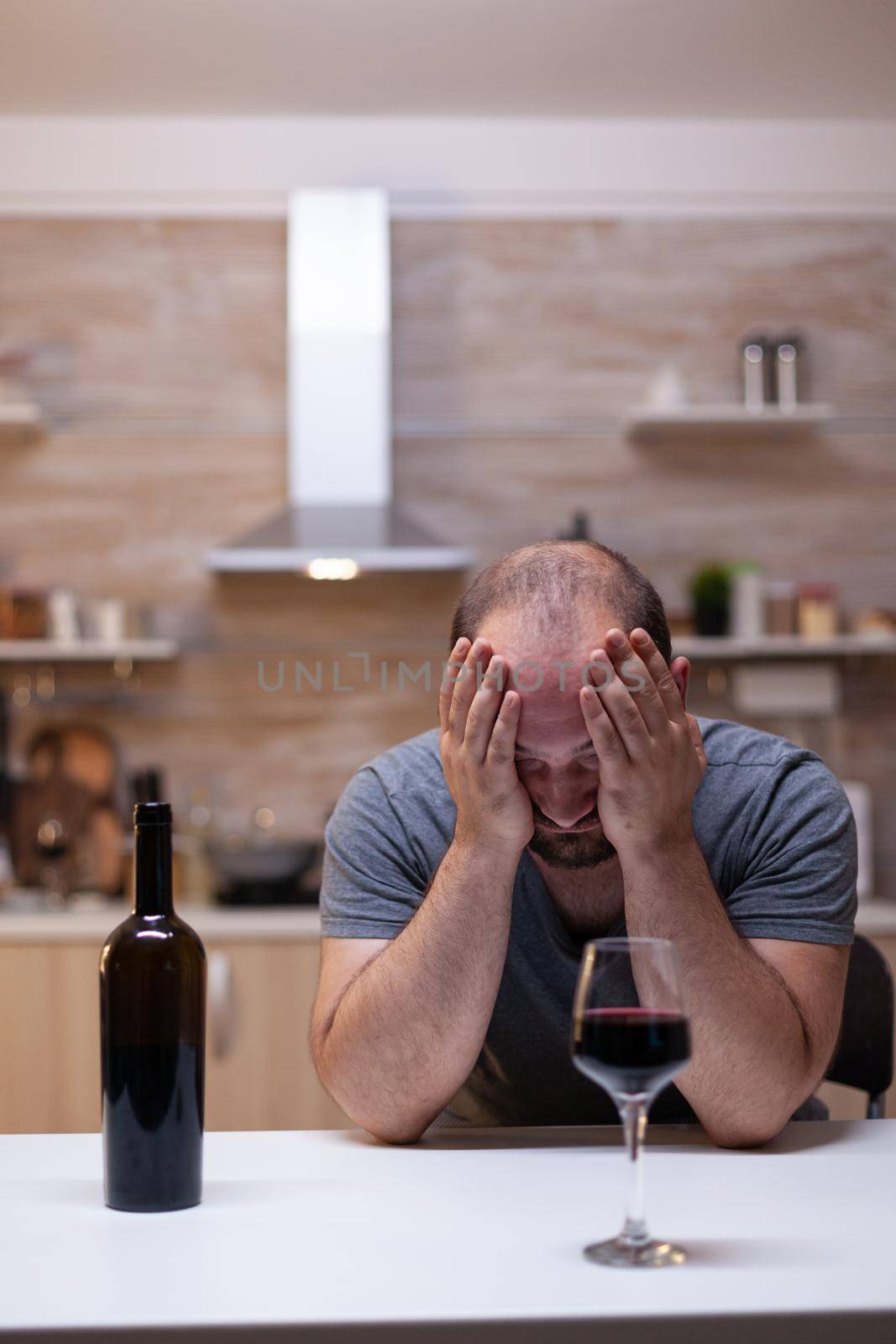 Desperate man feeling miserable while having glass with wine and bottle drinking alone. Person with unhealthy addiction sitting with liquor, booze, alcoholic beverage being upset