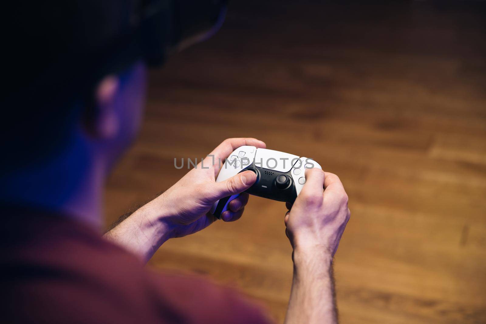 Closeup of man's hands playing video games on gaming console in front of TV widescreen. Man play with dual sense controller. Colorful lights