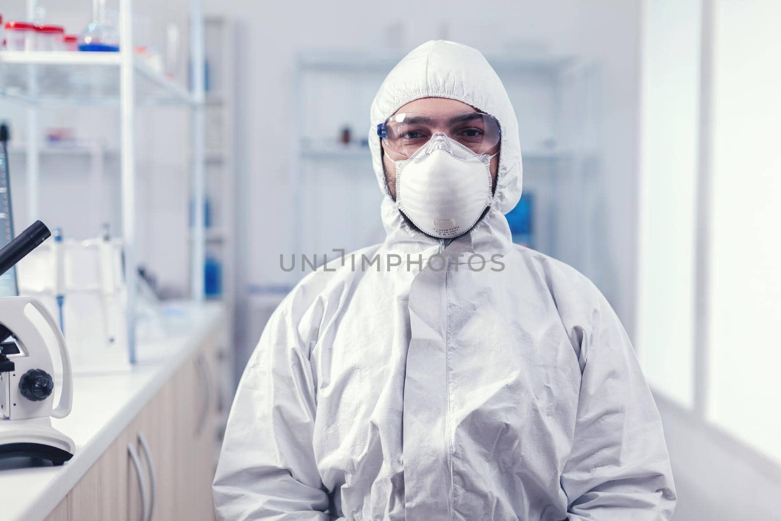 Portrait of tired scientist wearing coverall with protection glasses looking at camera in medicine laboratory. Overworked researcher dressed in protective suit against invection with coronavirus during global epidemic.