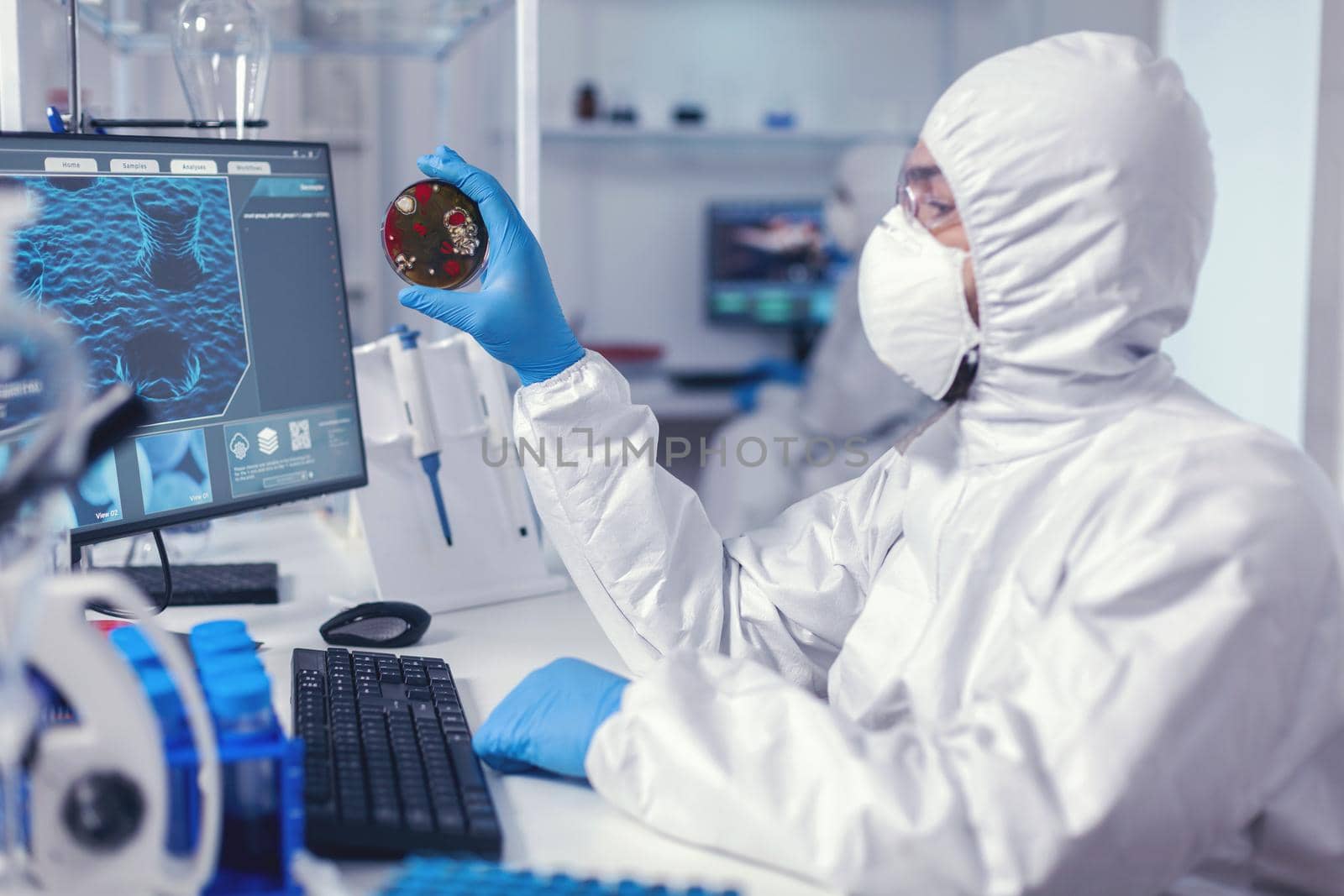 Scientist examining solution in petri dish in laboratory dressed in ppe suit. Doctors analysing vaccine evolution using high tech researching diagnosis against covid19 virus.