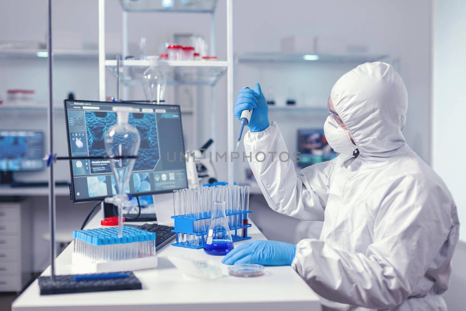 Researcher analyzing sample in automatic pipette working in lab dressed in coverall. Chemist in modern laboratory doing research using dispenser during global epidemic with covid-19.