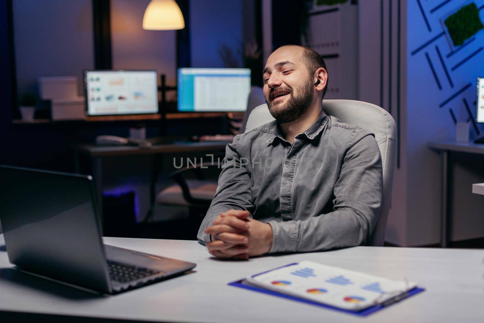 Financial specialist discussing about statistics during online call using laptop and wireless headphones. Businessman in the course of an important video conference while doing overtime at the office.