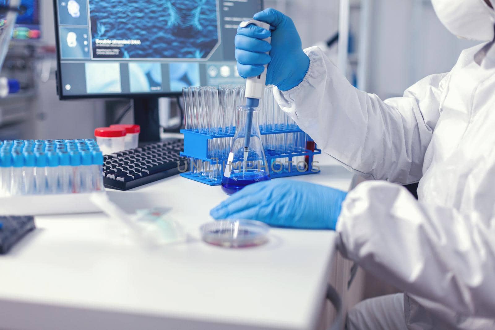 Medic in protective suit conducting test for coronavirus using automatic pipette. Chemist in modern laboratory doing research using dispenser during global epidemic with covid-19.