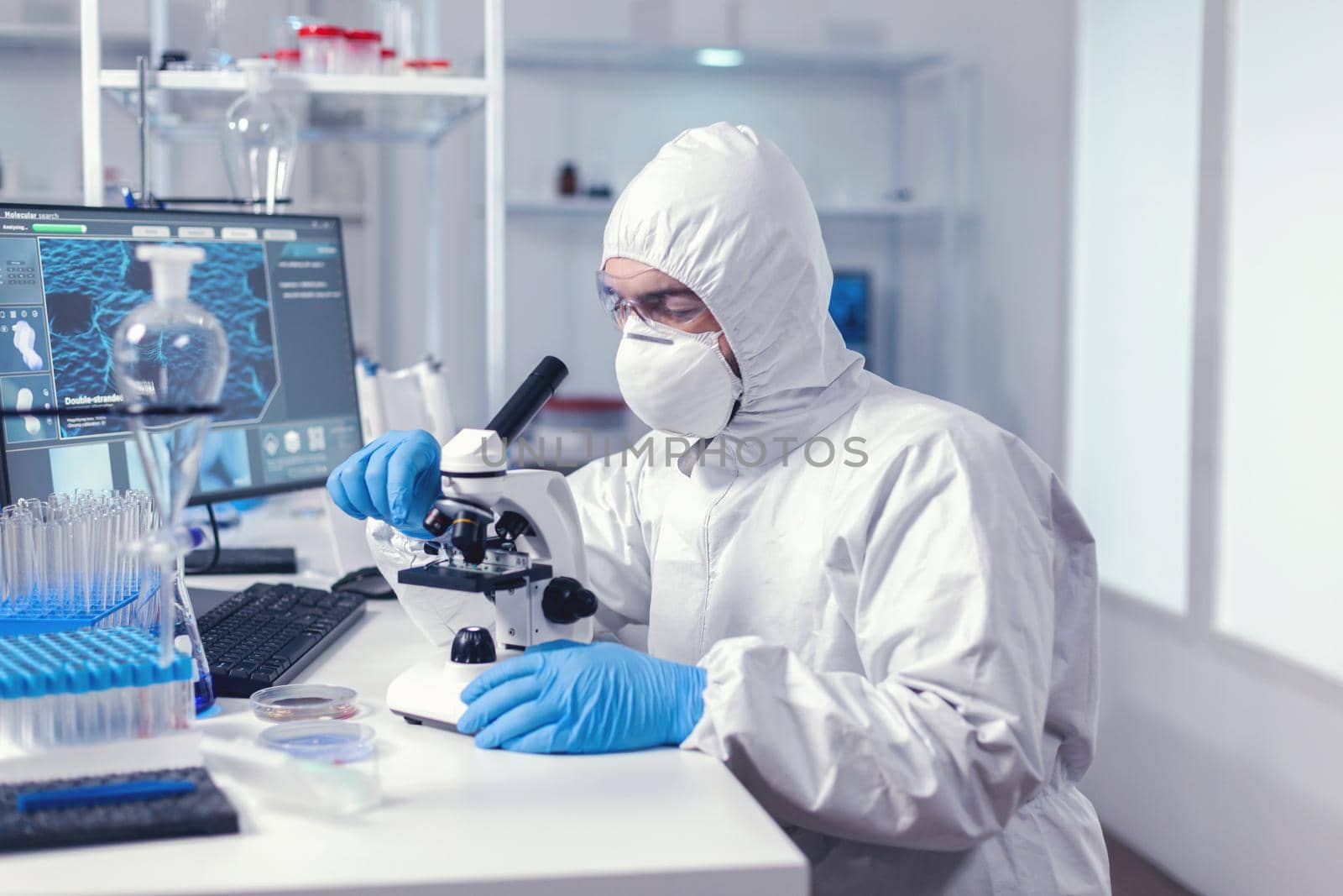 Doctor looking at sample of coronavirus using microscope in modern laboratory. Virolog in coverall during coronavirus outbreak conducting healthcare scientific analysis.