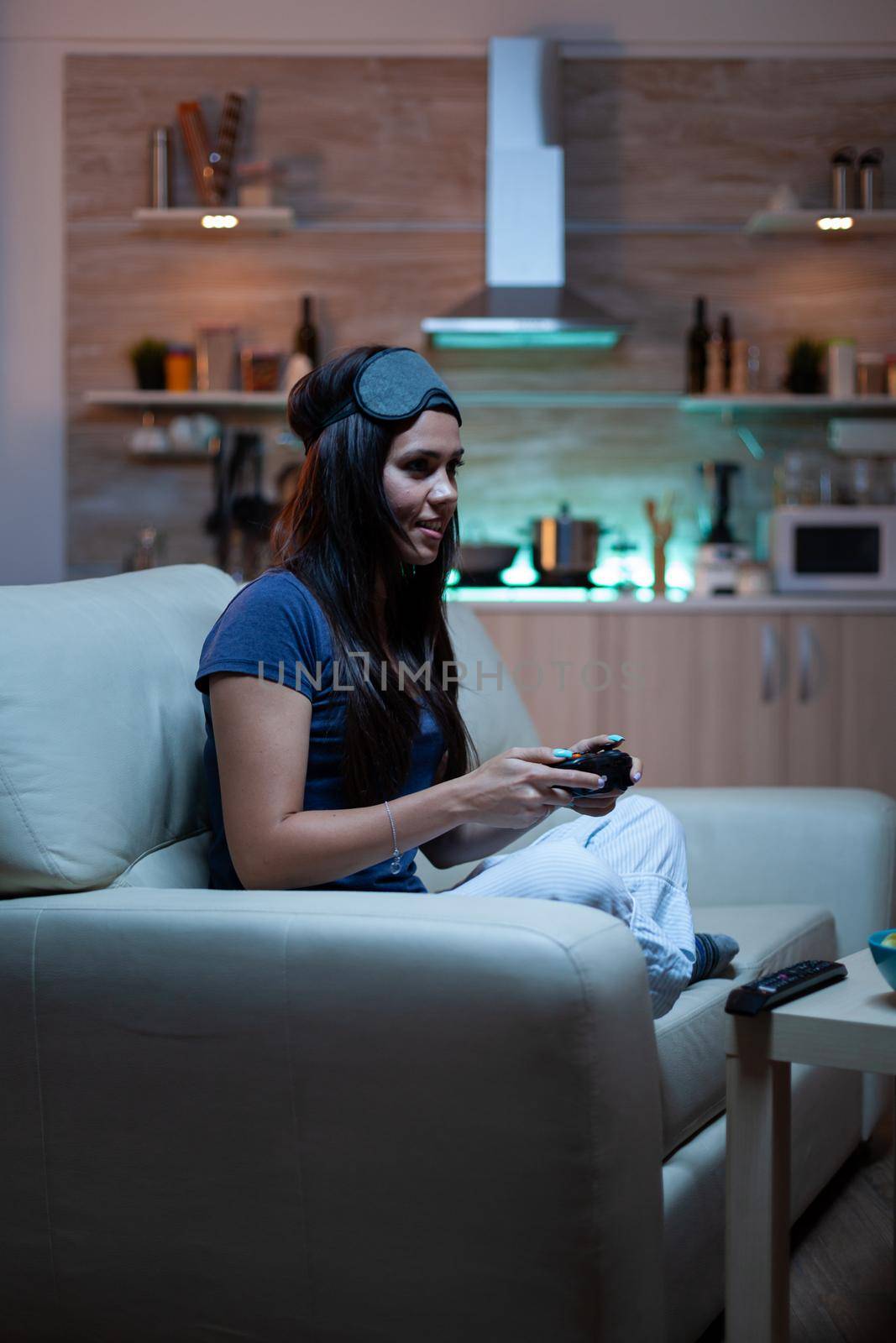 Gamer woman playing video games on console using controller and joysticks sitting on couch in front of TV. Excited determined person relaxing gaming with wireless controller having fun winning