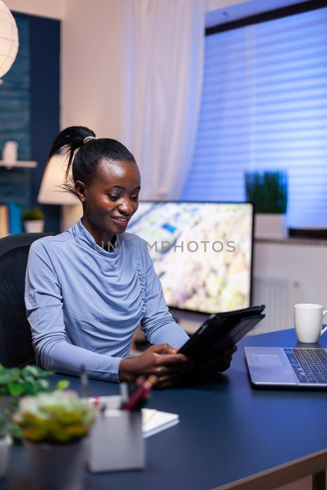 African business woman checking emails using tablet pc in the evening from home office. Busy focused employee using modern technology network wireless doing overtime writing.