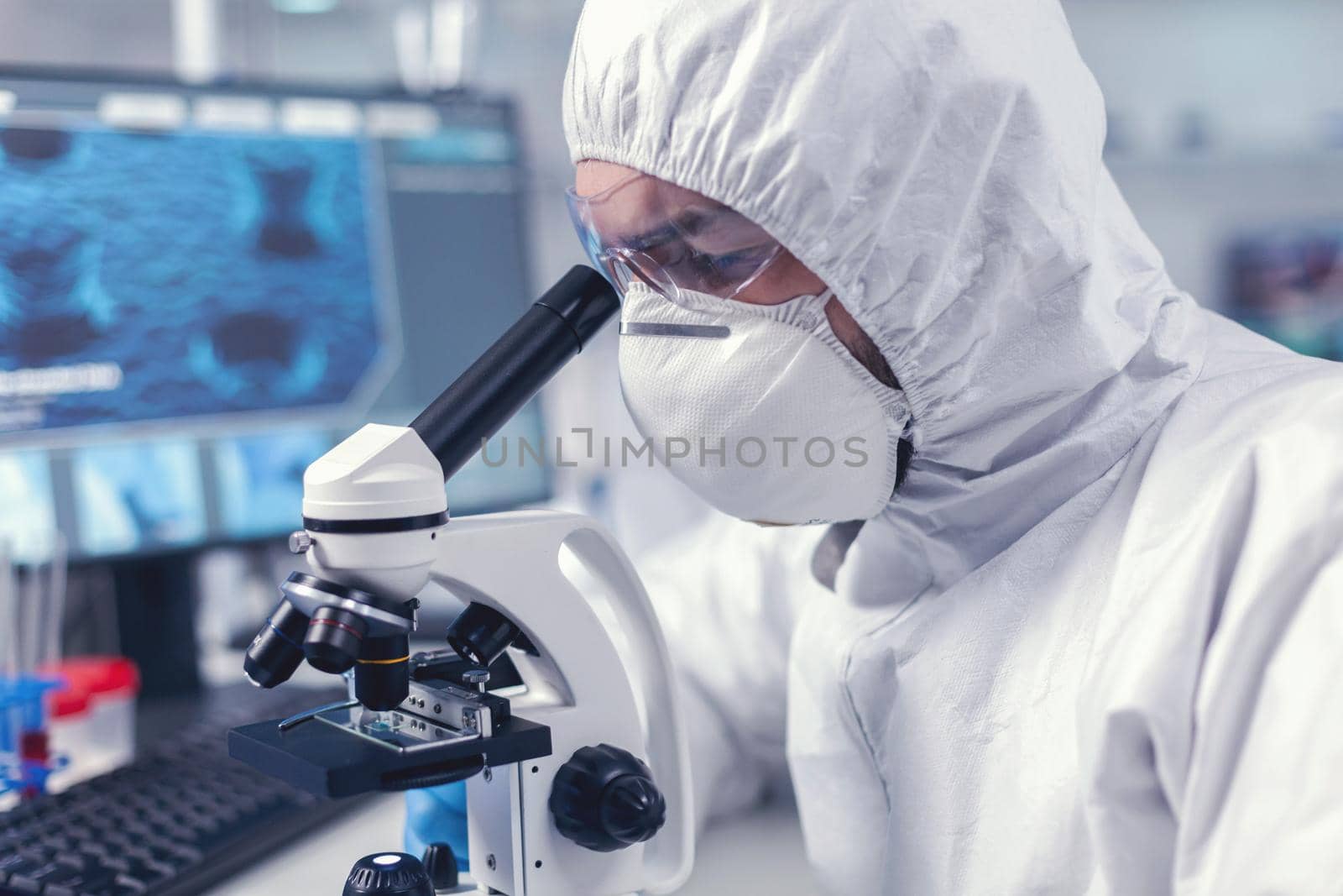 Close up of researcher looking throug microscope in biochemistry laboratory. Virolog in coverall during coronavirus outbreak conducting healthcare scientific analysis.