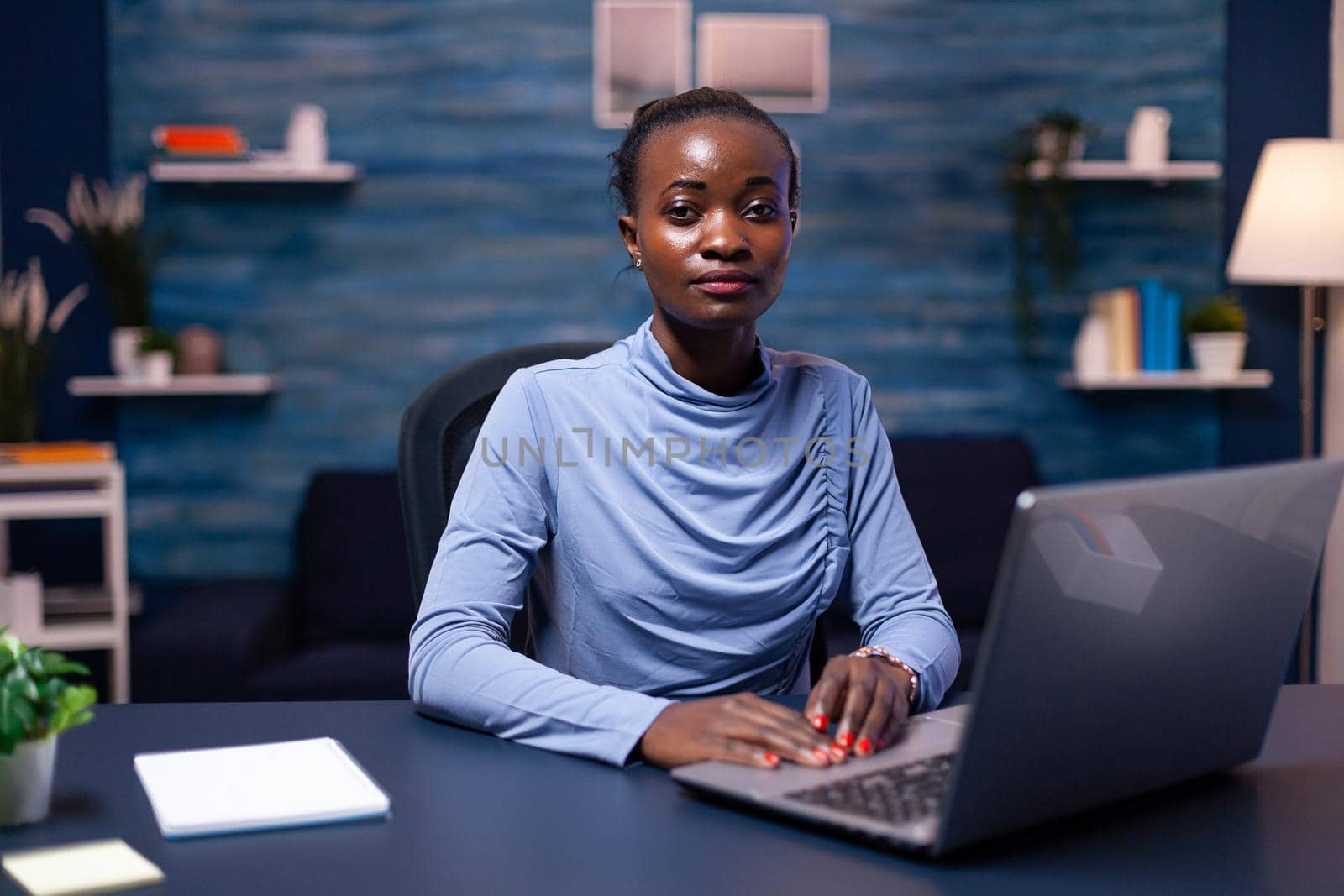 African businesswoman holding hands on keyboard while working from home late at night. Black entrepreneur sitting in personal workplace writing on keyboard.