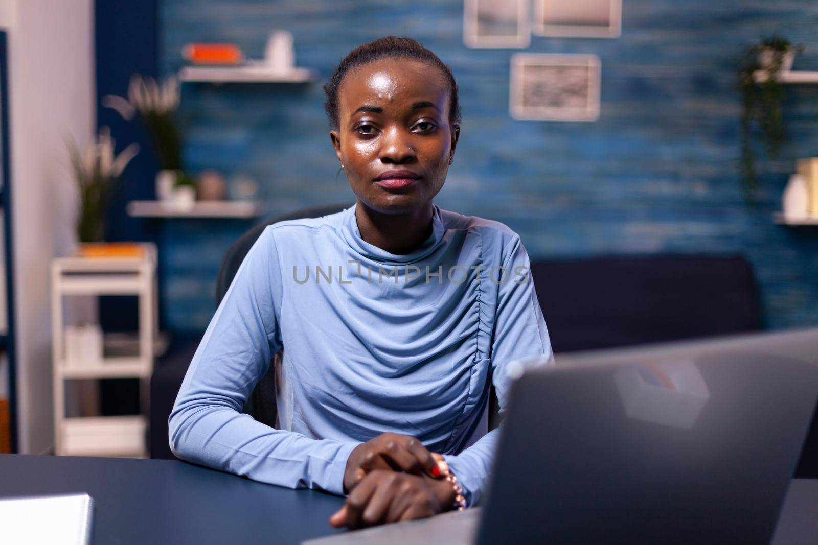 Portrait of dark skinned business woman working from cozy looking at camera working remote from home. Black entrepreneur sitting in personal workplace writing on keyboard.