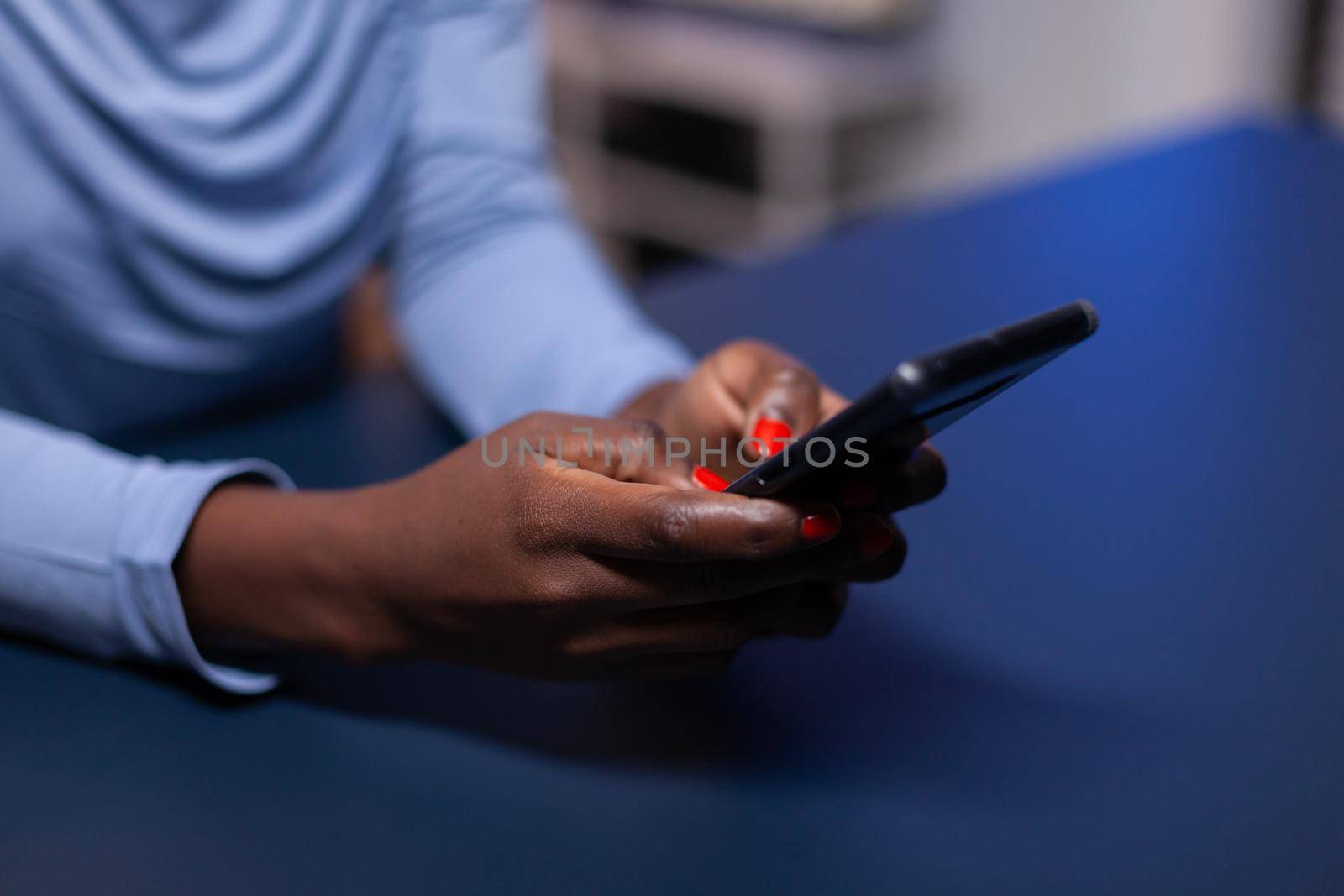 Close up of dark skinned business woman browsing on smartphone from home in the evening. Employee using modern technology network wireless doing overtime.