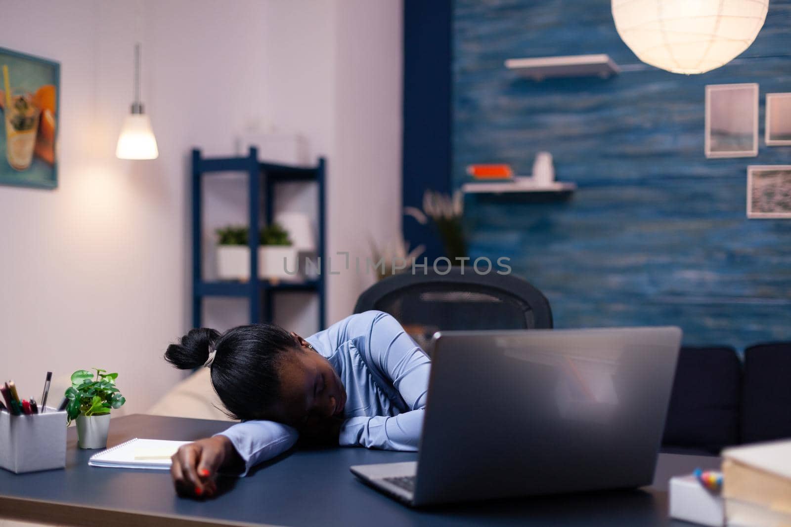 African business woman sleeps during late night hourse in the course of deadline working from home. Busy employee using modern technology network wireless doing overtime sleeping on table.
