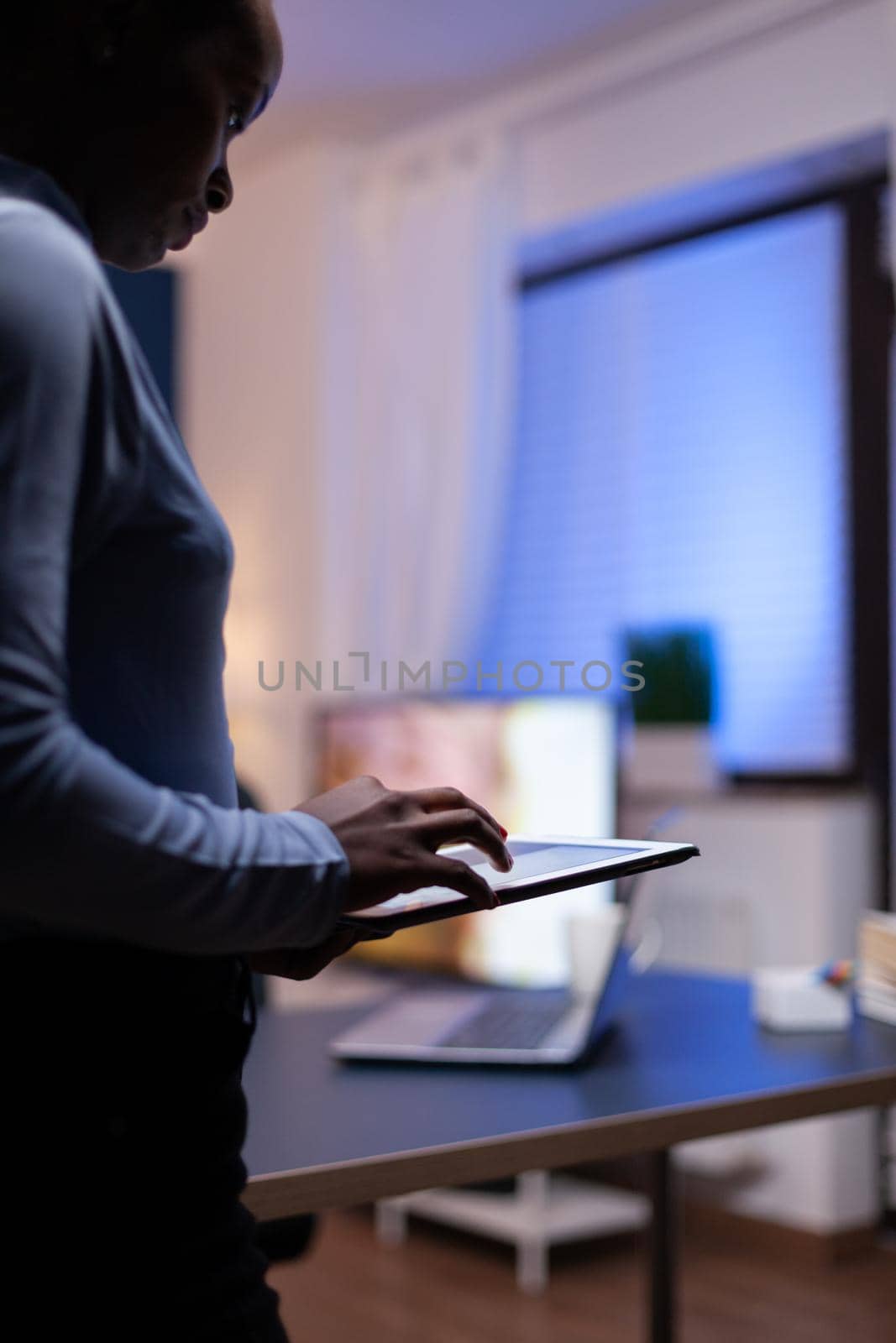 Dark skinned woman using tablet pc keybpad to write email working from home office. Busy focused employee using modern technology network wireless doing overtime writing.