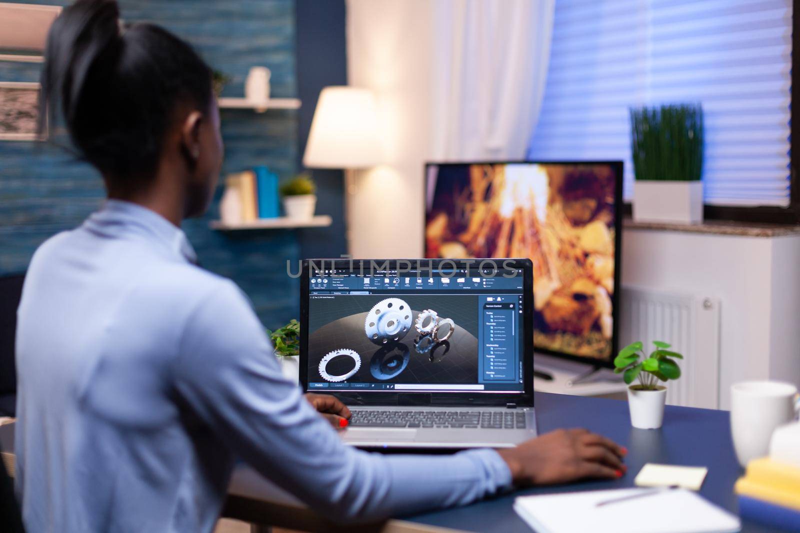 African freelancer using cad to design a technical concept from home office in the evening. Industrial black female engineer studying prototype idea on personal computer showing software on device display