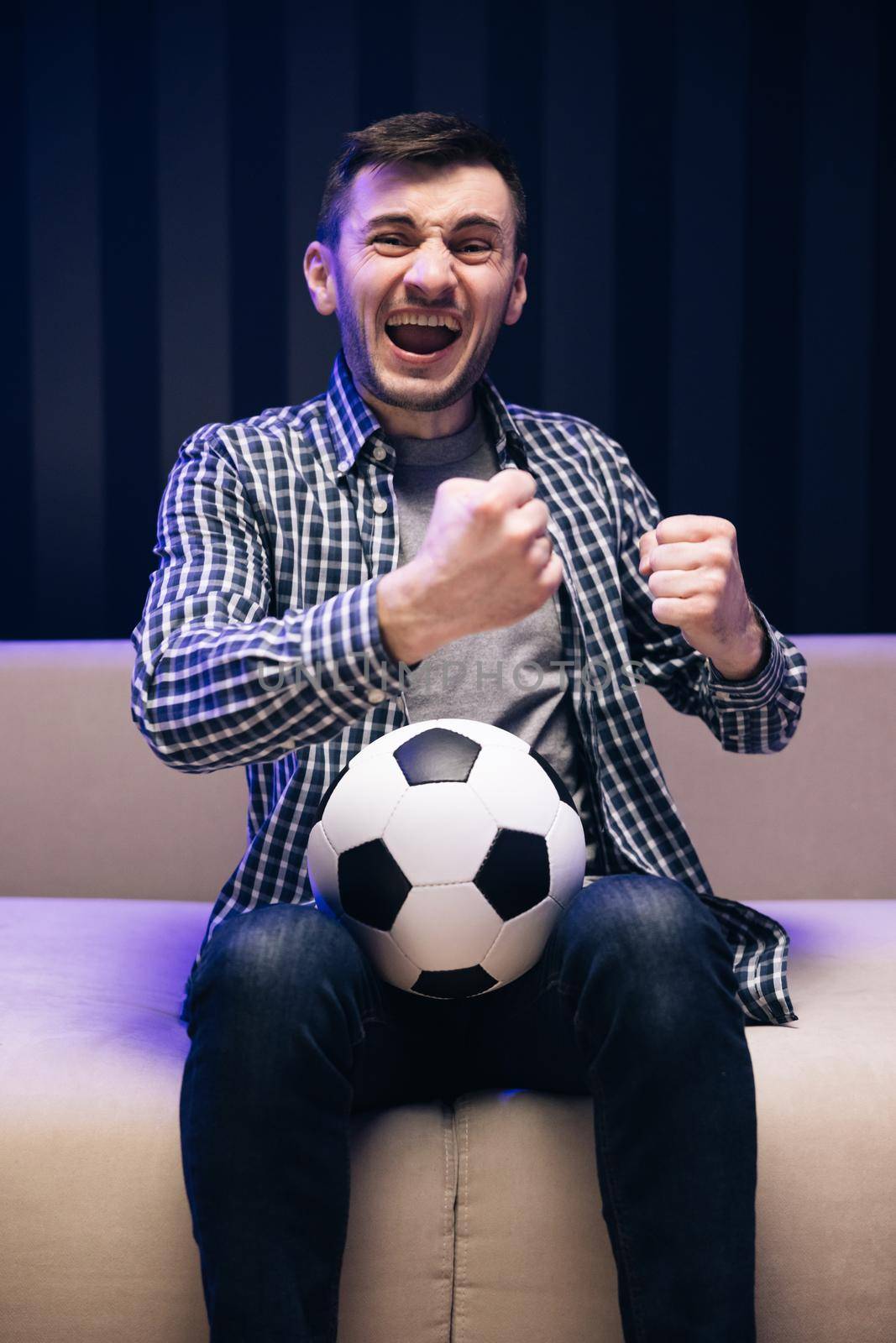Gladly Surprised Reaction Of A Young Man Is Watching Tv And Sitting On The Sofa. Sports Fan Reaction Concept. Excited sports fan watching his favourite player on TV. Football fan watching championship by uflypro