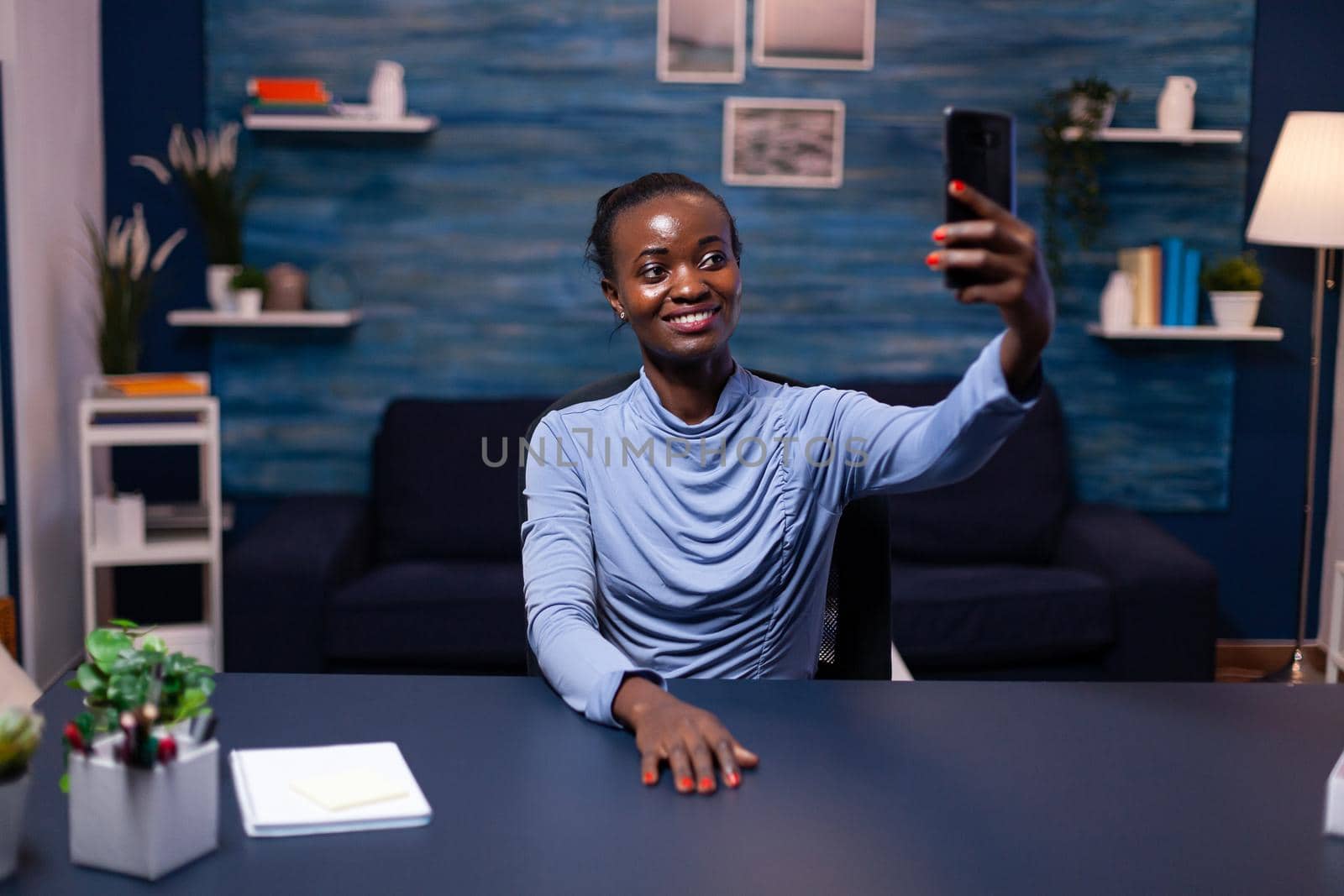 Happy african looking at smartphone taking selfie looking at front camera. Busy focused freelancer using modern technology network wireless doing overtime.