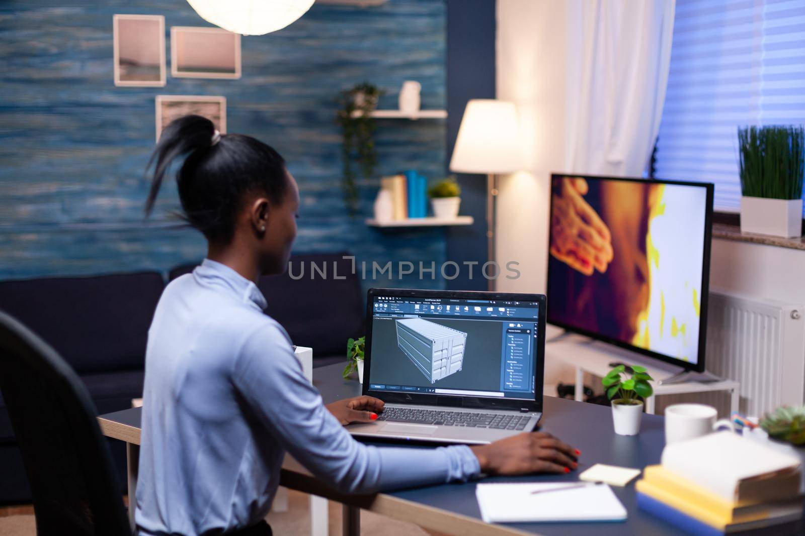 African entrepreneur developer working from home office late at night. Industrial black female engineer studying prototype idea on personal computer showing software on device display