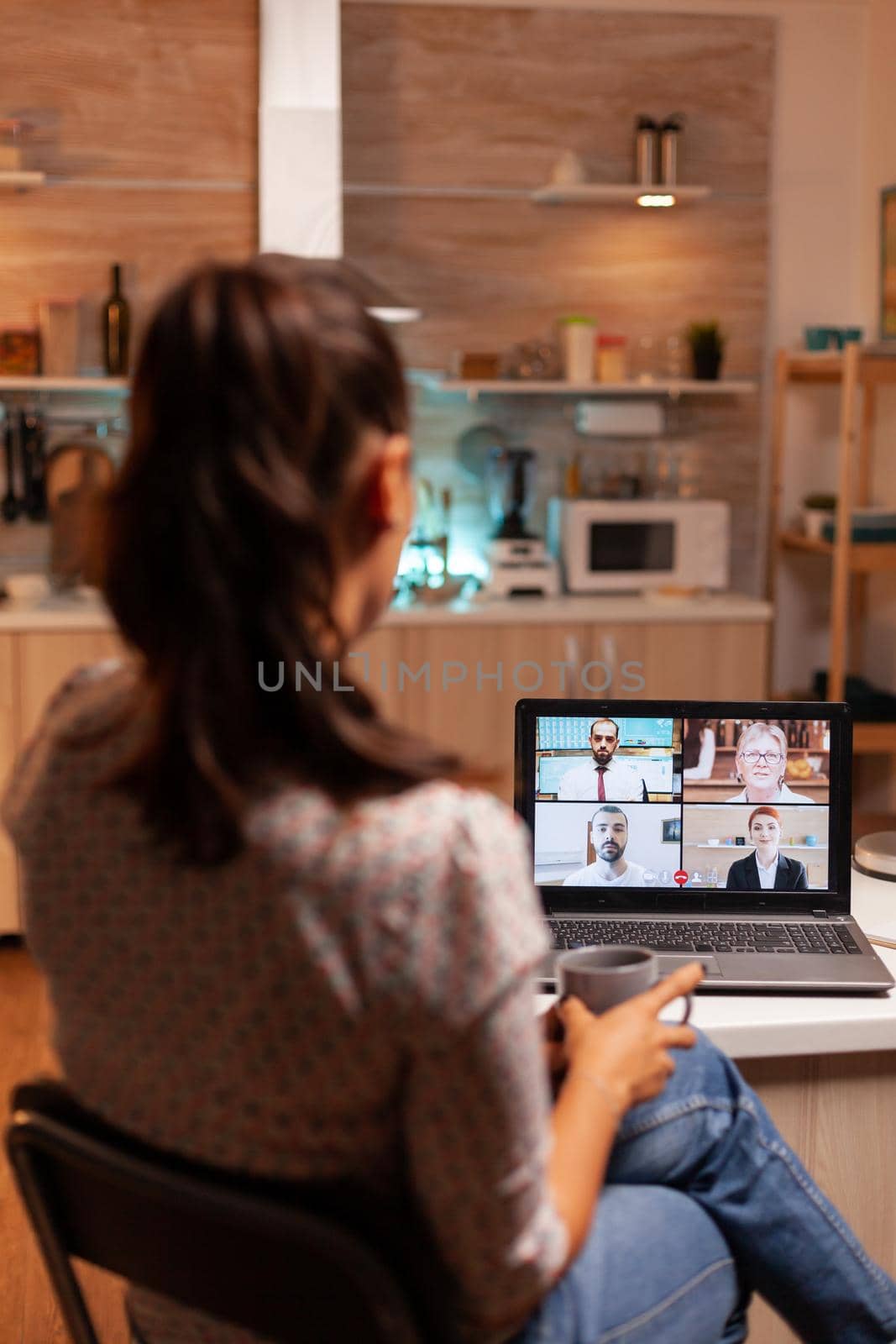 Woman talking with coworkers during video conference at midnight from home holding a cup of coffee. Corporate meeting using modern technology, laptop late at night , tech, agency, advisor, work, discussion.