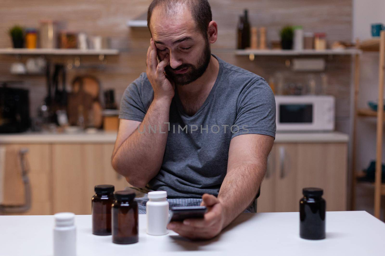 Caucasian man with headache looking at smartphone by DCStudio