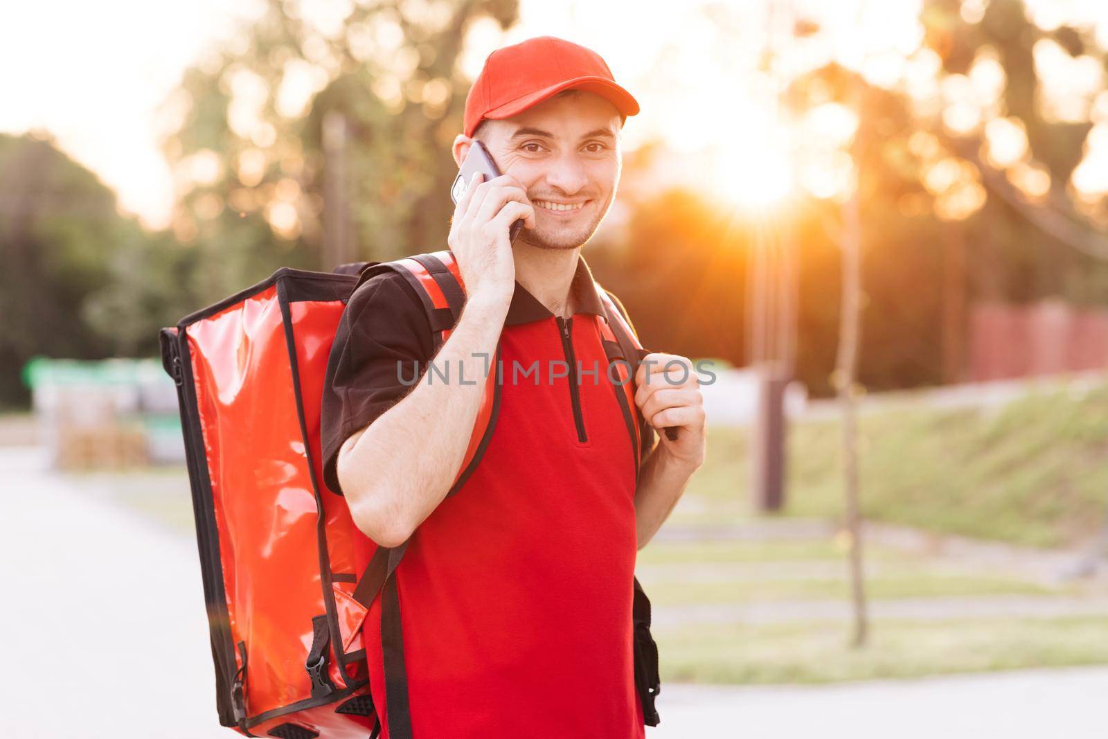 Food delivery guy with red backpack deliver orders. Male courier with isothermal food case box arrives to the entrance to the house and calls for client.