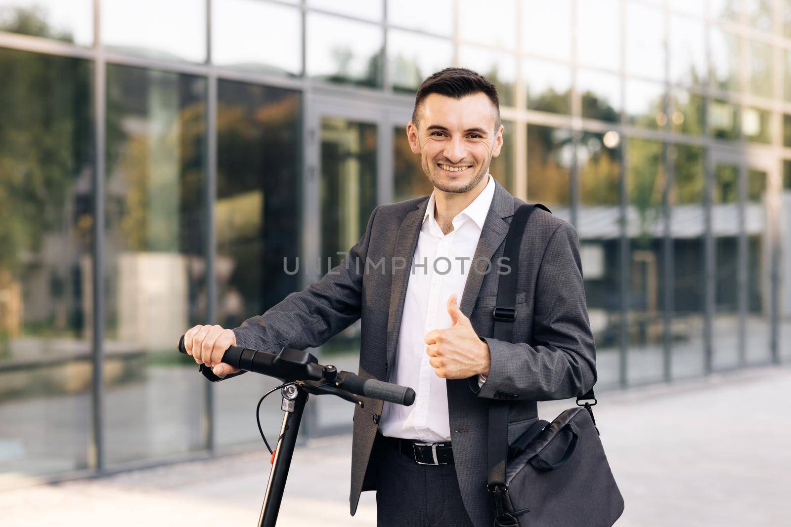 Portrait of caucasian businessman leaning on electric scooter and looking at camera. Stylysh man on vehicle outdoors. Eco-friendly modern urban transport. Ecology and urban lifestyle by uflypro