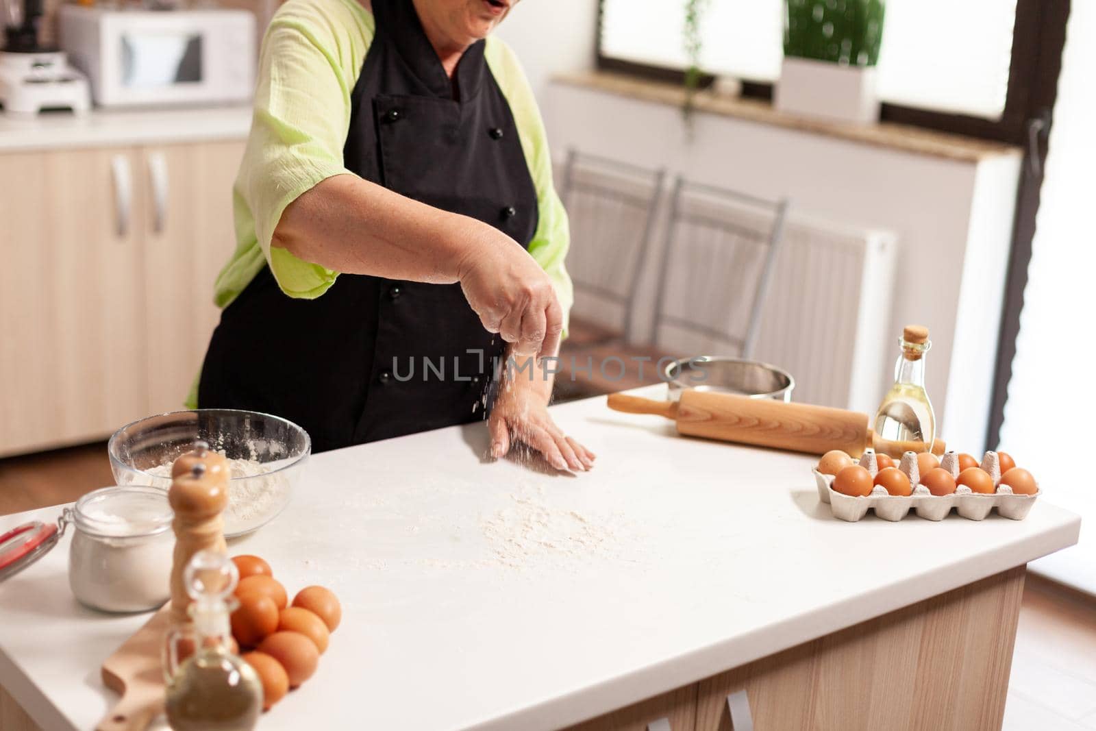Grandmother preparing homemade donuts wearing kitchen apron. Retired senior chef with bonete and apron, in kitchen uniform sprinkling sieving sifting ingredients by hand baking homemade pizza and bread
