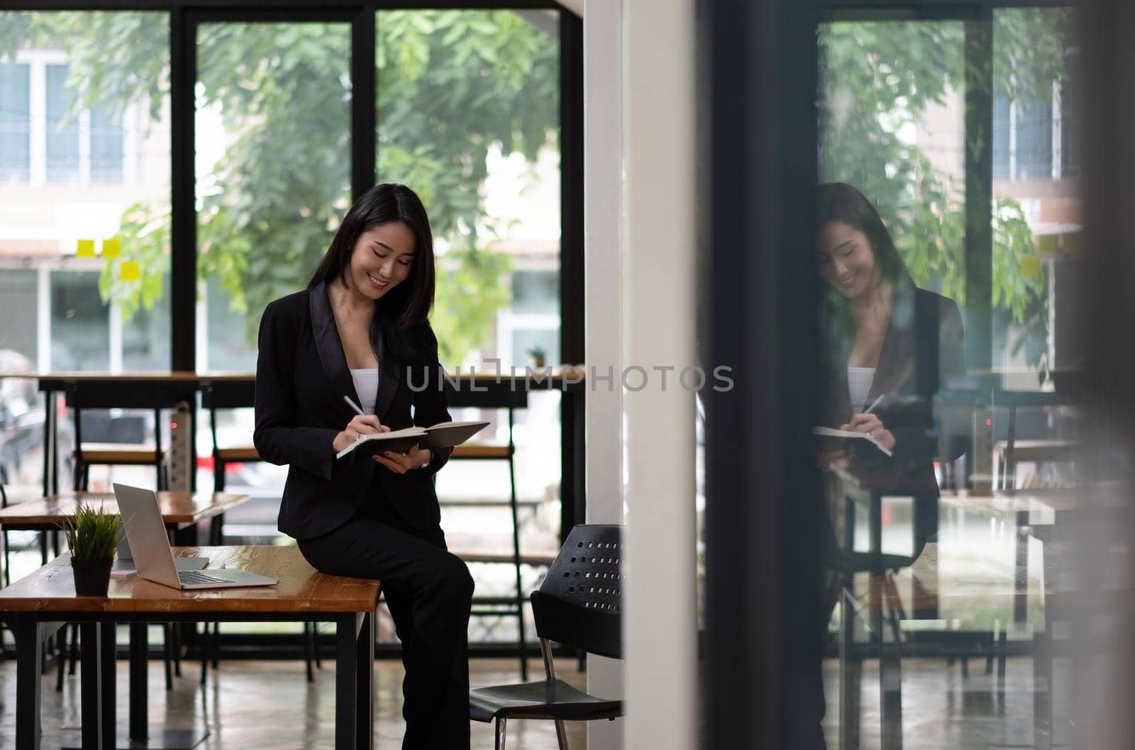 Portrait of beautiful smiling young entrepreneur businesswoman working with laptop computer during taking note on notepad.