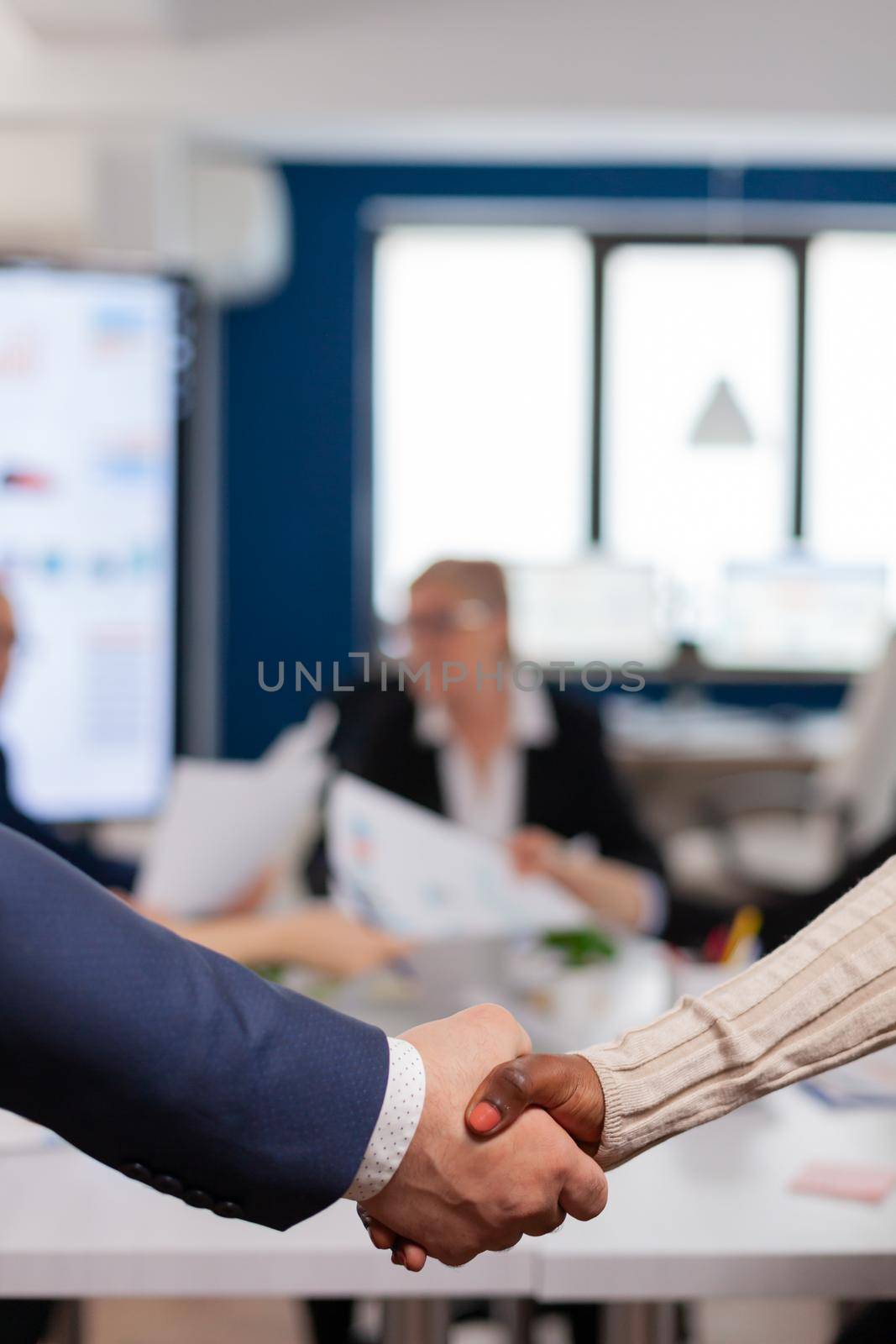 Close up of multiracial business partners standing in front of conference desk shaking hands after signing partnership contract. Diverse team being happy for successful negotiations in startup company