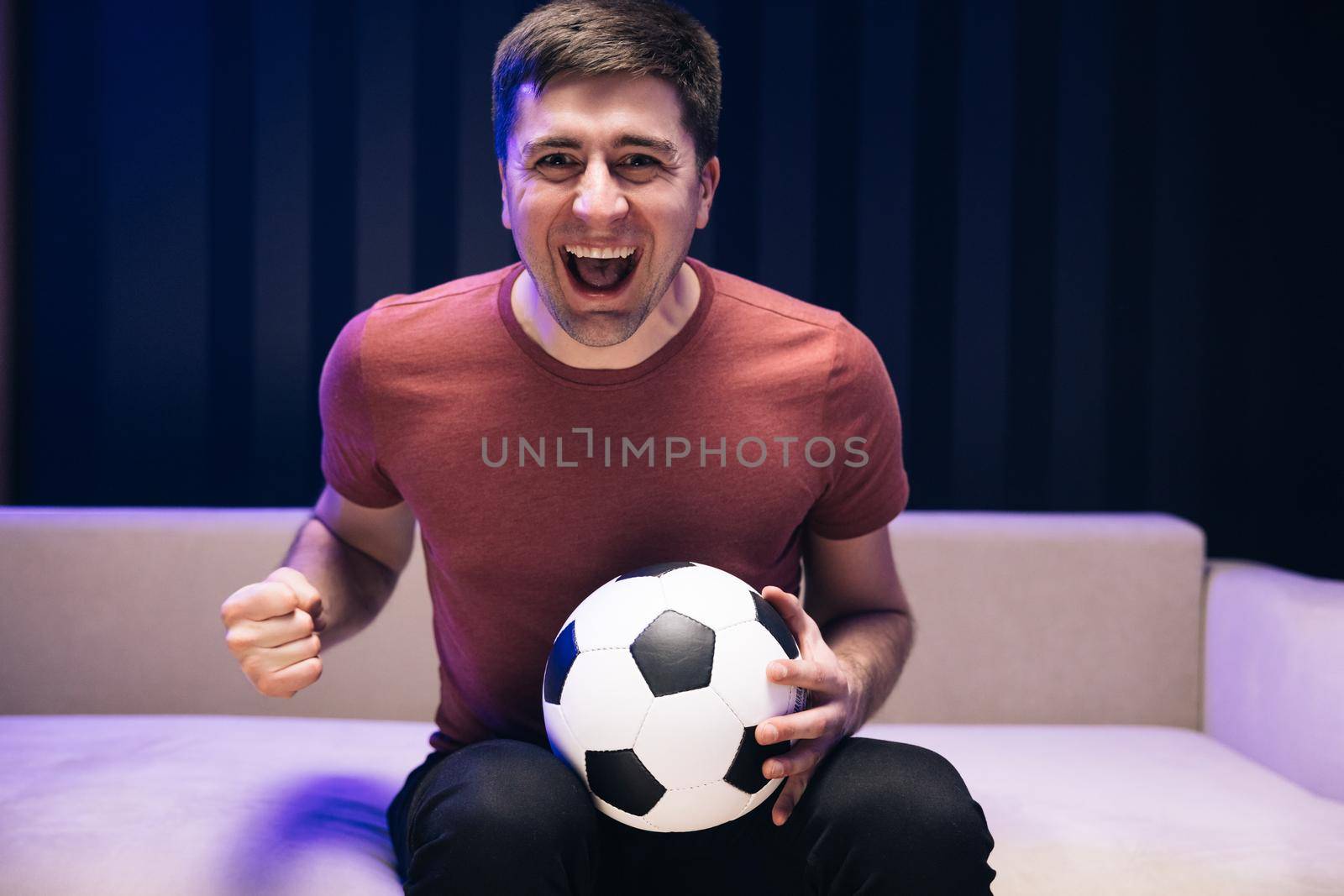 Football fan watching championship. Excited sports fan watching his favourite player on TV. Gladly Surprised Reaction Of A Young Man Is Watching Tv And Sitting On The Sofa. Sports Fan Reaction Concept by uflypro