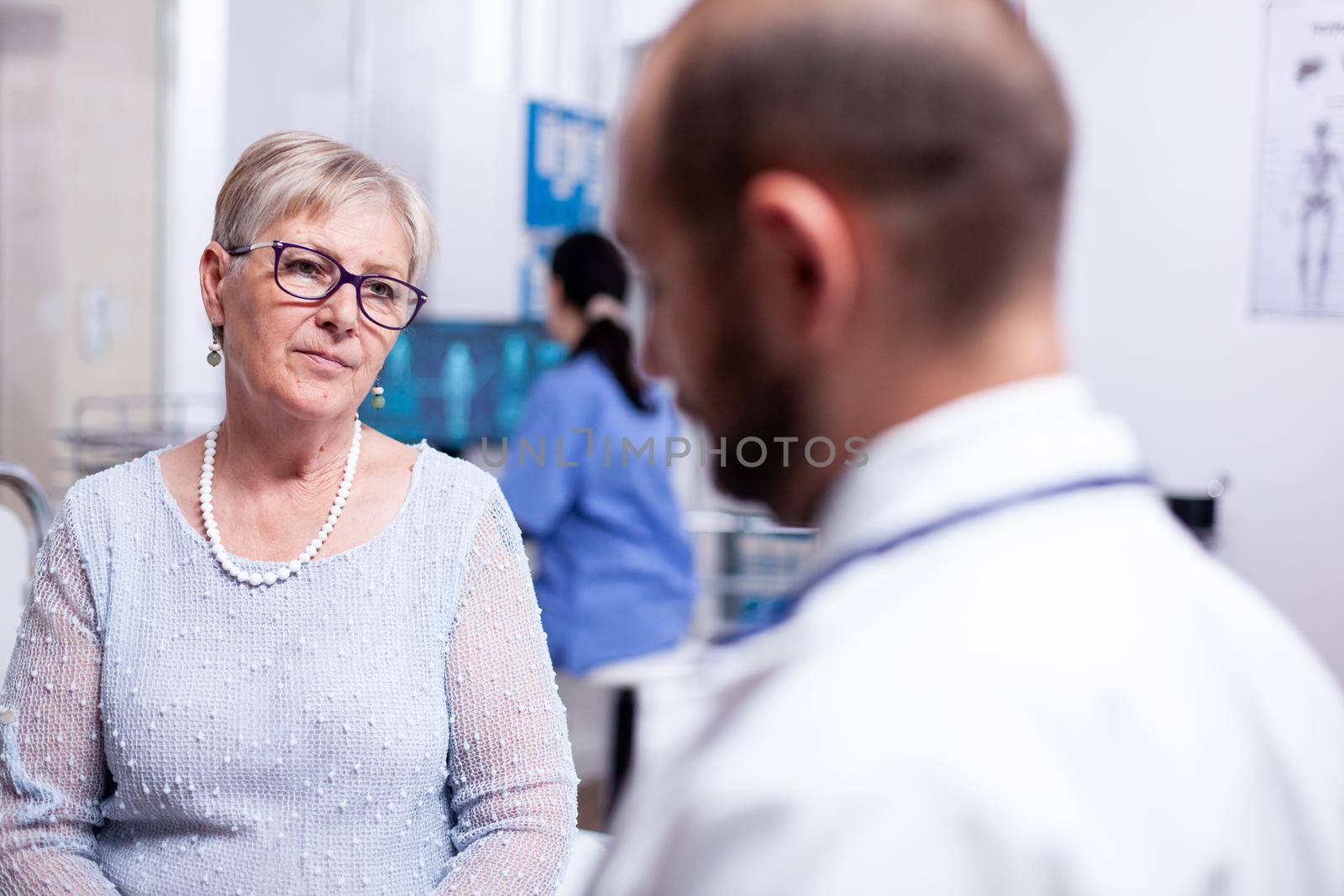 Woman listening doctor during examination in consultation clinic room. Converstation with medical stuff clinic medicine healthcare, senior, coat, clipboard.