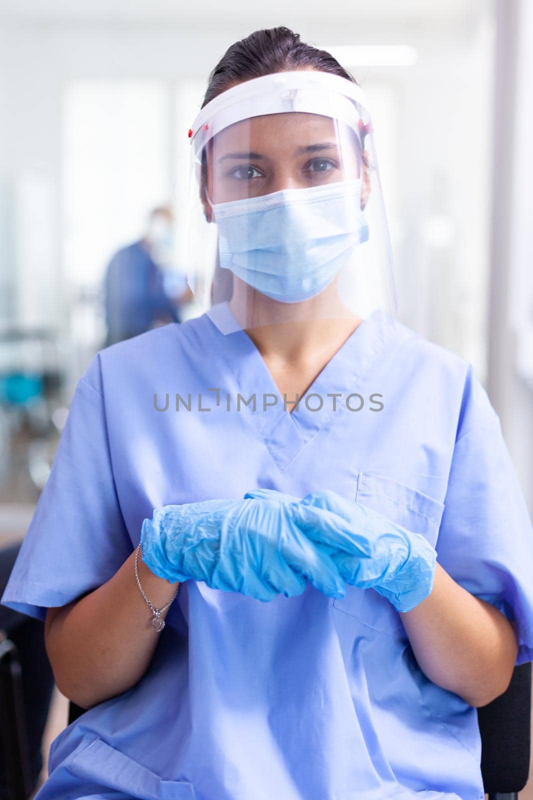 Medical assistant with visor and face mask tired in hospital waiting room during coronavirus outbreak. Doctor consulting senior man in examination room. Physician, epidemic, care, surgical, corridor.