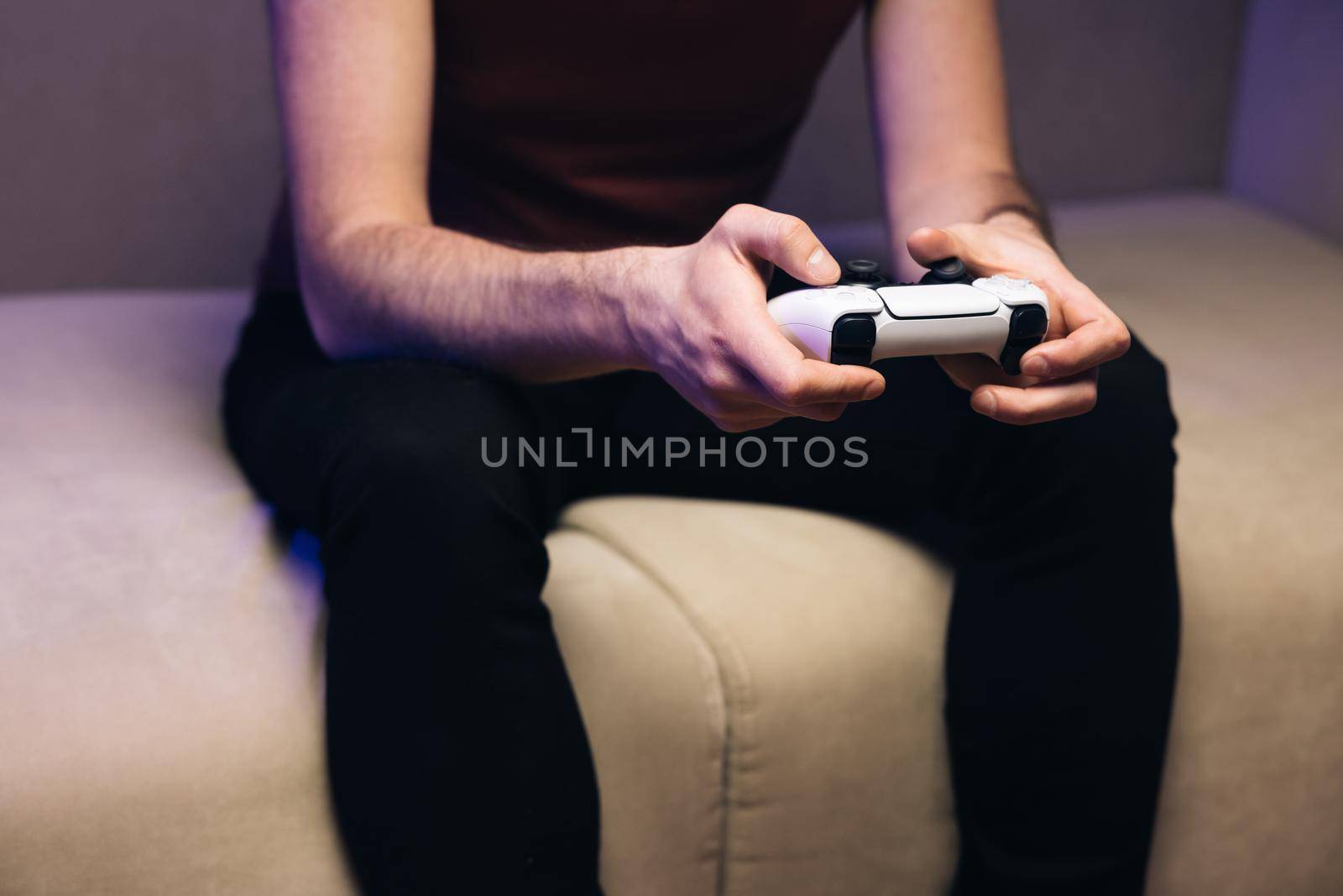 Close-up of the man holding a white joystick next gen console and playing a video game on TV. Males hands holding joystick, playing video game and having fun.
