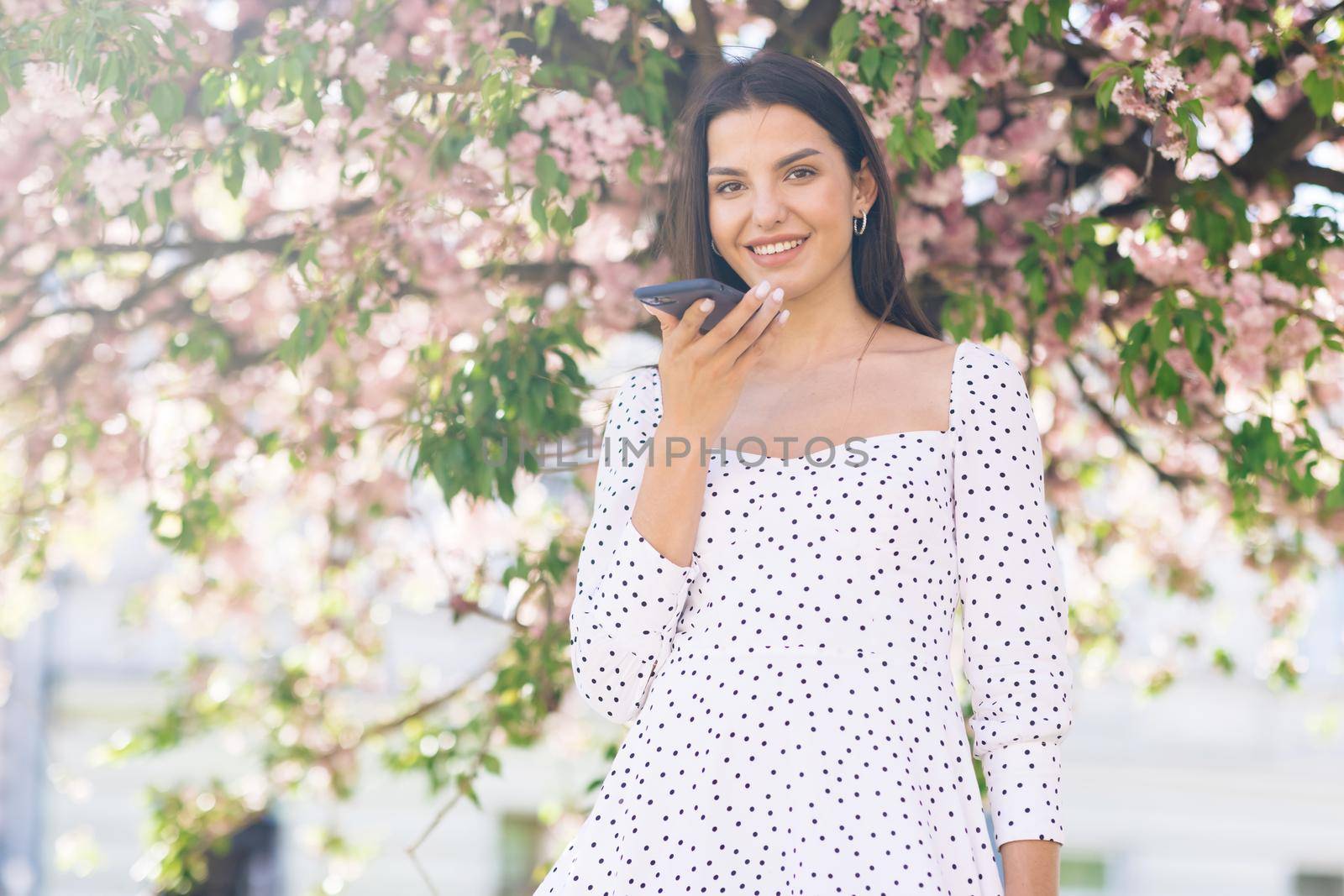 Woman using a smart phone voice recognition function online walking on a city street, talking to mobile assistant. Girl using smartphone voice recognition, dictates thoughts, voice dialing message by uflypro