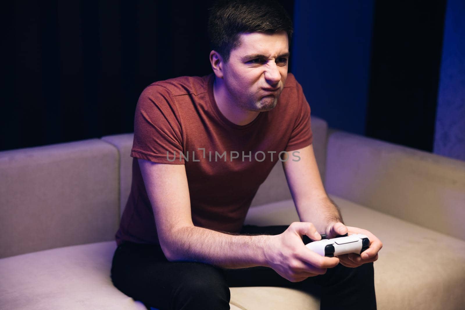 Handsome young man enjoying free time alone while sitting on couch in living room. Caucasian guy playing video game and using joystick by uflypro