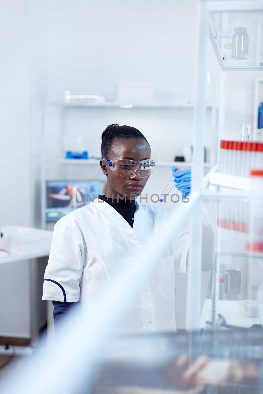 African scientist examining blue liquid in genetic laboratory. Black researcher in sterile laboratory conducting pharmacology experiment wearing coat.