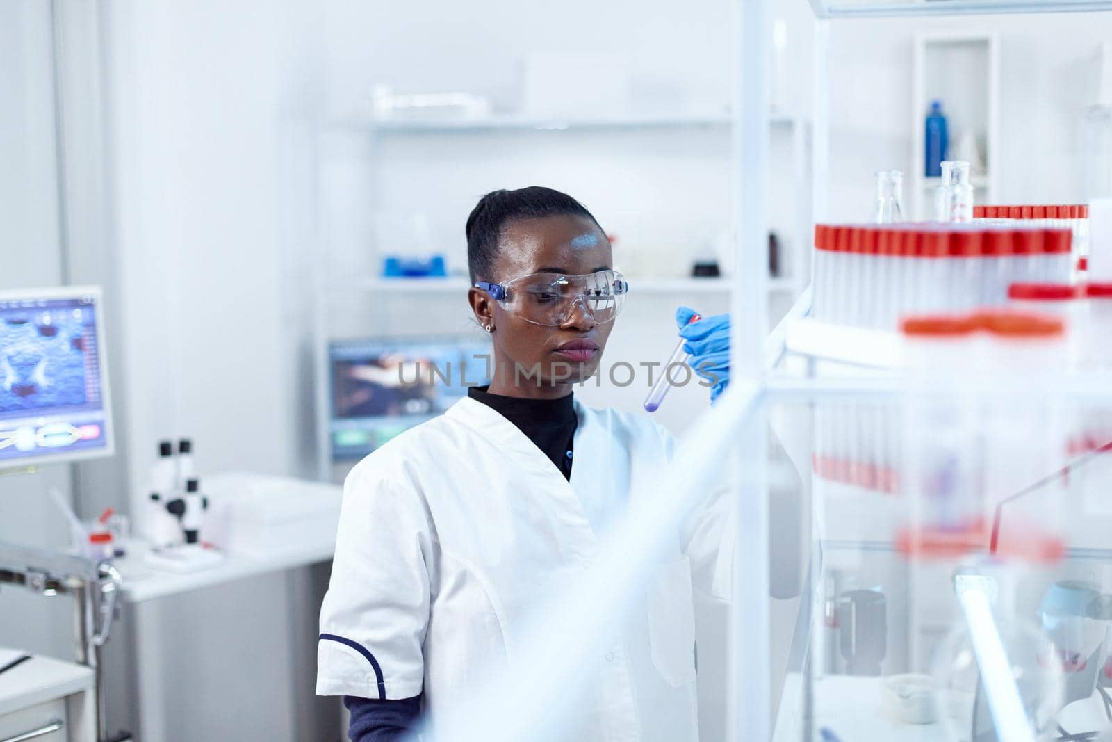 African scientist in protective glasses looking at test tube by DCStudio